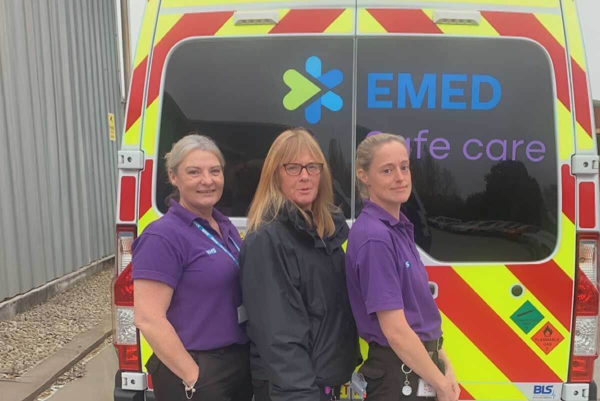 Three EMED Safe Care team members in uniform standing proudly in front of an EMED Safe Care ambulance